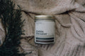Candle labeled 'Cabin Sweater' on a textured fabric background