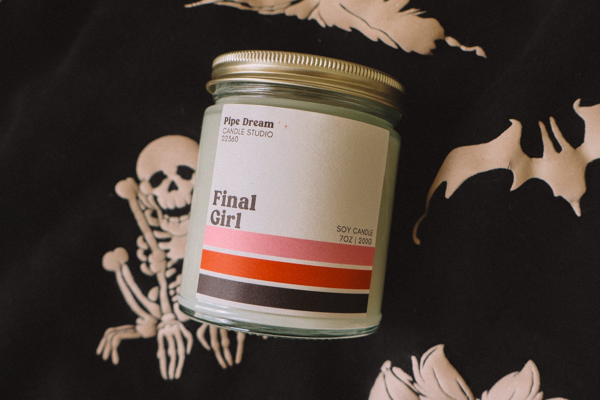 A candle labeled Final Girl staged on top of a black and white ghost sweatshirt.