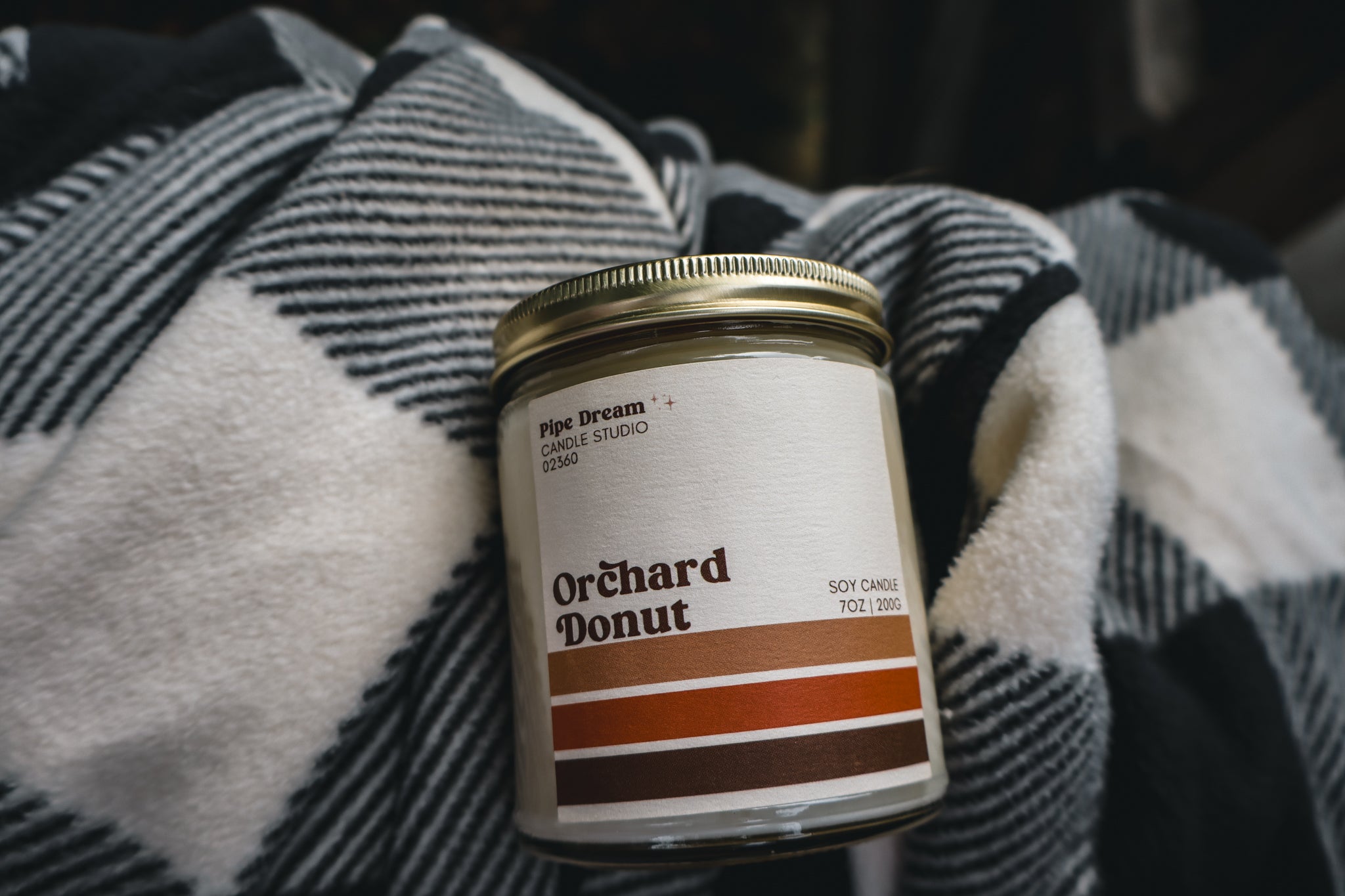 Candle labeled 'Orchard Donut' on a flannel background