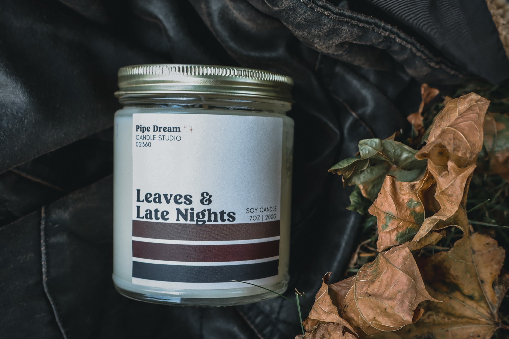 Candle jar labeled 'Leaves & Late Nights' lain on a leather jacket  with leaves.