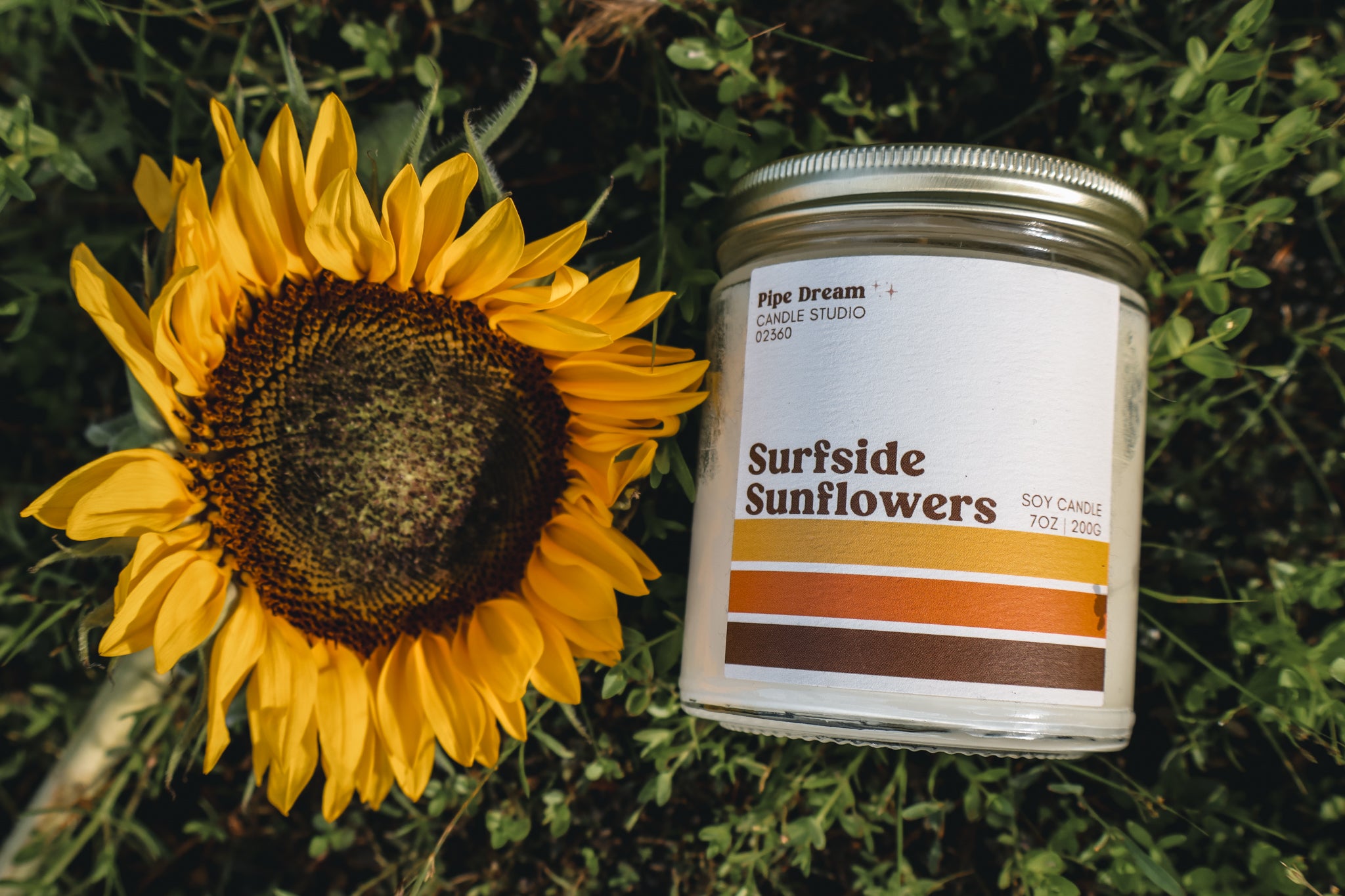 Candle labeled 'Surfside Sunflowers' next to a sunflower on grass. 