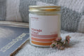A jar candle with a label reading 'Vintage Vinyl' placed on a surface with a record and dried flowers nearby.